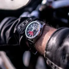 Mężczyzna w skórzanej kurtce i rękawicach motocyklowych sprawdza czas na zegarku Edifice. Czerwony akcent na tarczy dodaje mu charakteru.