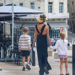 Kobieta w letniej sukience i kapeluszu prowadzi dwójkę dzieci, chłopca i dziewczynkę, ulicą. To francuskie dziecko, które zwiedza miasto.
