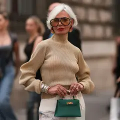 Elegancka kobieta z siwymi włosami i okularami w stylu retro, trzymająca zieloną torebkę. Jej styl pokazuje, że pewne rzeczy nigdy nie są passe.