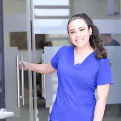 Uśmiechnięta pielęgniarka w niebieskim uniformie otwiera drzwi. Czy zastanawiasz się, ile zarabia pielęgniarka pediatryczna?
