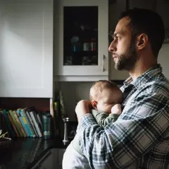 Tata po francusku, czyli "papa", czule tuli swoje śpiące dziecko w kuchni.