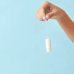 Dłoń trzyma tampon. To produkt higieniczny, który po angielsku nazywa się "tampon".