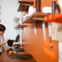 Mężczyzna pracuje w swoim atelier, tworząc skórzane wyroby. Na stole narzędzia i materiały.