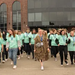 Grupa młodych ludzi w zielonych koszulkach idzie przed budynkiem. Zastanawiasz się, ile kosztuje szkoła w chmurze?