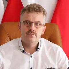 Starosta w okularach i białej koszuli, siedzący przed polskimi flagami, wygląda jakby właśnie skończył wykład o tym, co robi starosta na studiach.