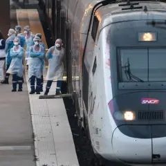Grupa osób w kombinezonach ochronnych stoi na peronie obok pociągu SNCF.
