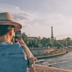Kobieta w kapeluszu robi zdjęcie Wieży Eiffla nad Sekwaną. Idealne wakacje po francusku.