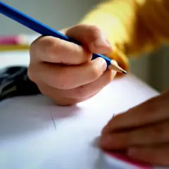 Dziecko pisze kredką, licząc ile dni do końca szkoły. Obok leżą nożyczki.