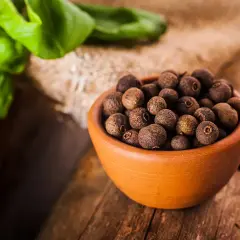 Miseczka pełna ziaren ziela angielskiego, jednego z aromatycznych spices po polsku, na drewnianym blacie.