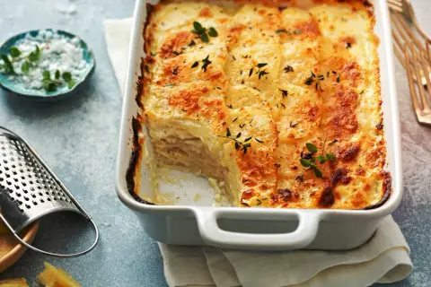 Złocisty ziemniak au gratin, czyli zapiekany pod serem i śmietaną, kusi aromatem. Obok tarka i zioła.