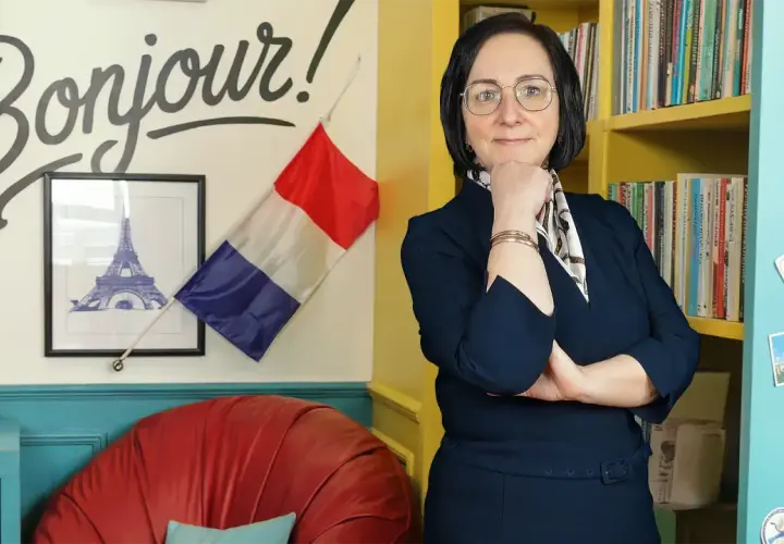 Kobieta w okularach, otoczona francuskimi akcentami, jak "Bonjour!" i flaga. Uczy zaimków wskazujących francuski.
