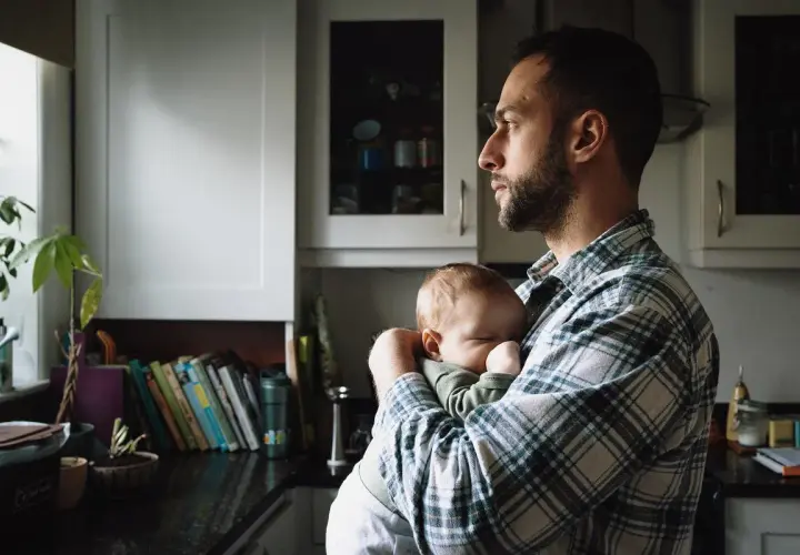 Tata po francusku, czyli "papa", czule tuli swoje śpiące dziecko w kuchni.