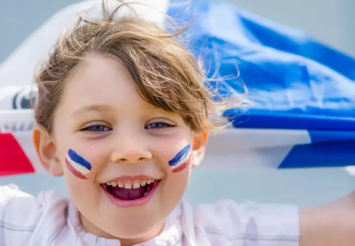 Uśmiechnięta Agnieszka z francuskimi barwami na policzkach, trzymająca flagę Francji.