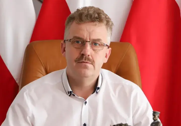 Starosta w okularach i białej koszuli, siedzący przed polskimi flagami, wygląda jakby właśnie skończył wykład o tym, co robi starosta na studiach.