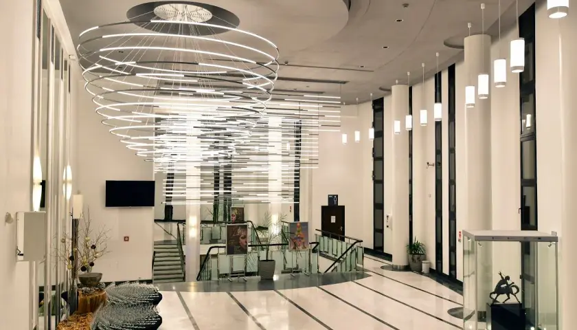 Nowoczesny, przestronny foyer z imponującą, wielopoziomową lampą i szklaną gablotą z rzeźbą.
