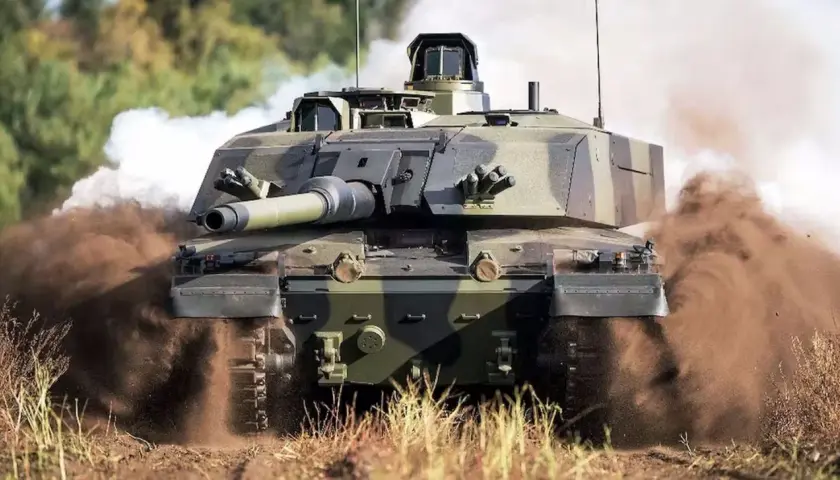 Challenger 2, potężny czołg, pędzi przez teren, wzbijając tumany kurzu i dymu.