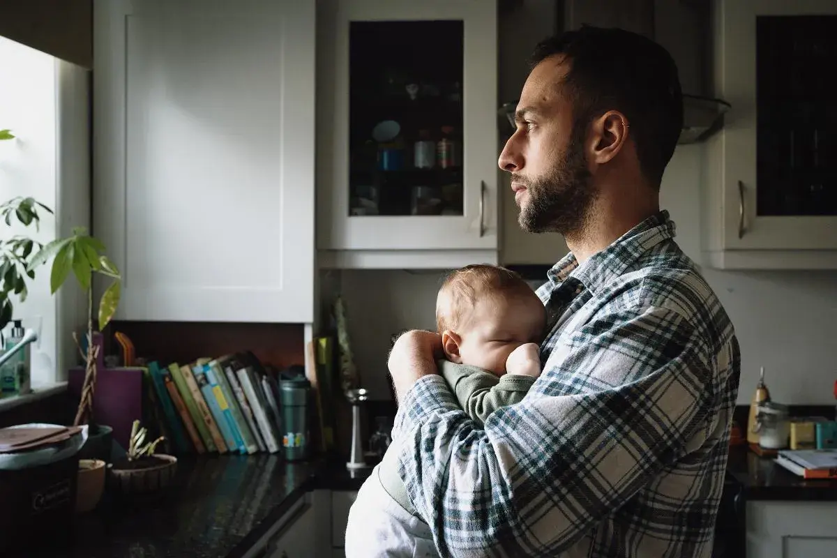 Tata po francusku, czyli "papa", czule tuli swoje śpiące dziecko w kuchni.