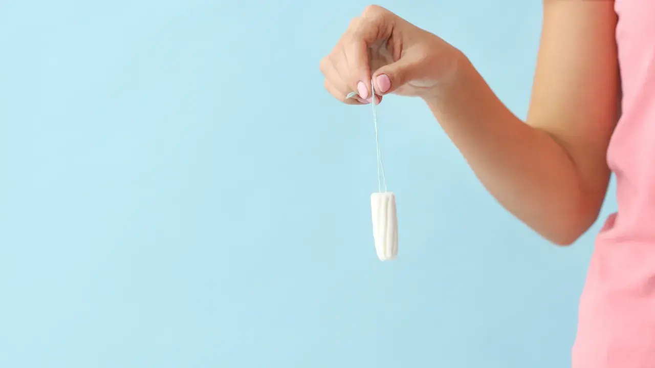 Dłoń trzyma tampon. To produkt higieniczny, który po angielsku nazywa się "tampon".