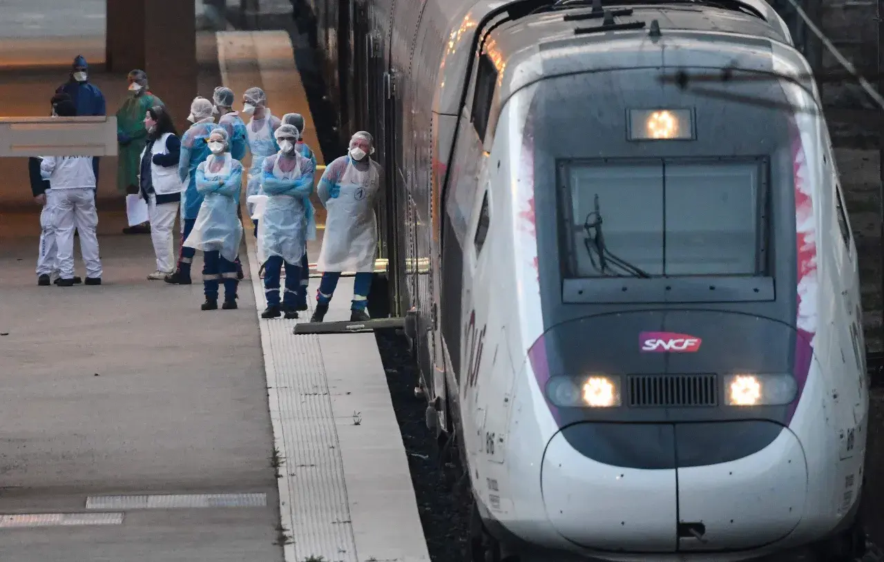 Grupa osób w kombinezonach ochronnych stoi na peronie obok pociągu SNCF.