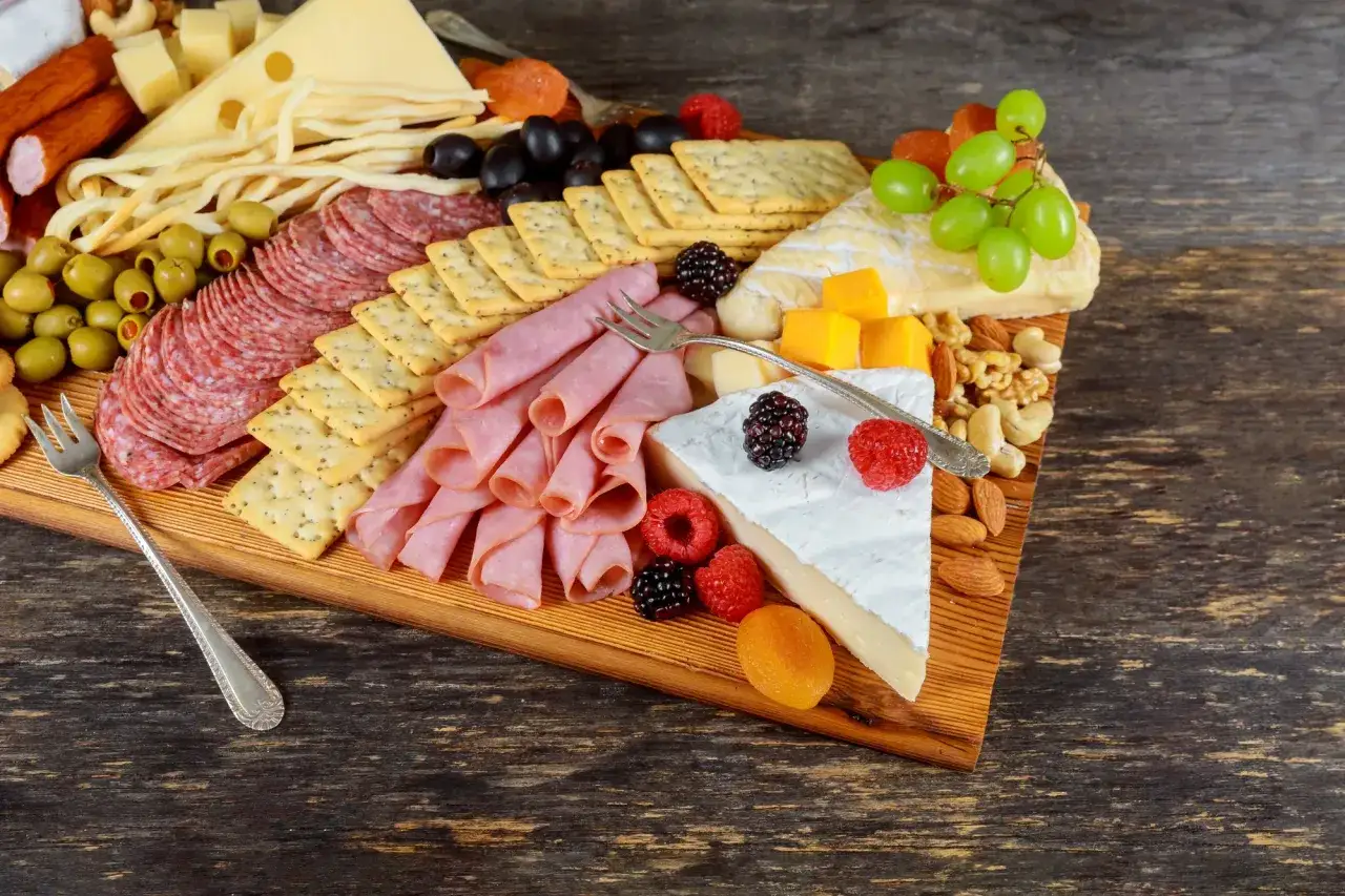 Wykwintna deska serów i wędlin, czyli polska charcuterie: sery, kiełbaski, szynka, oliwki, winogrona, orzechy i owoce.