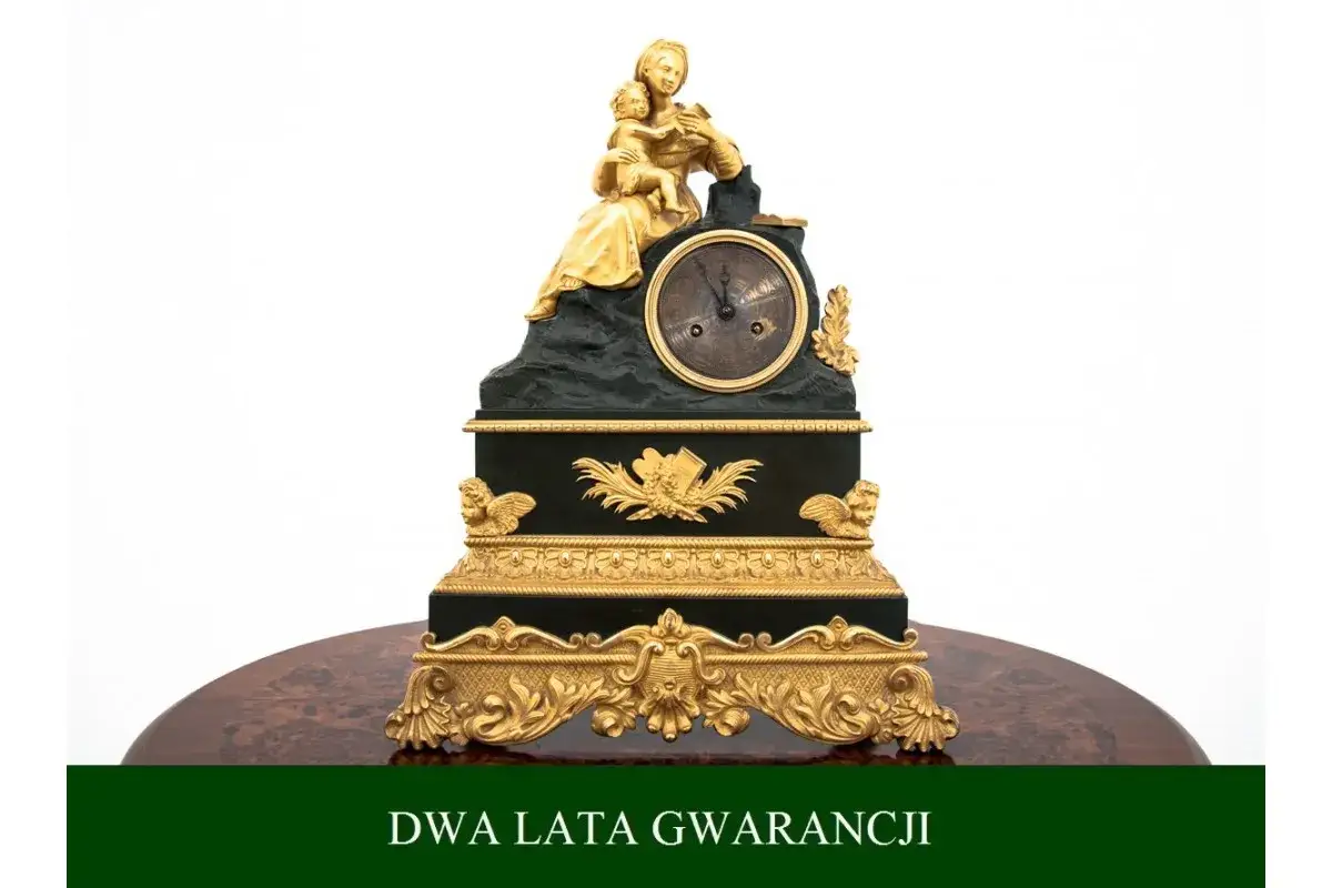 Elegancka, złocona figura kobiety z dzieckiem na szczycie czarnego zegara. To piękna godzina po francusku, ozdobiona aniołkami i ornamentami.