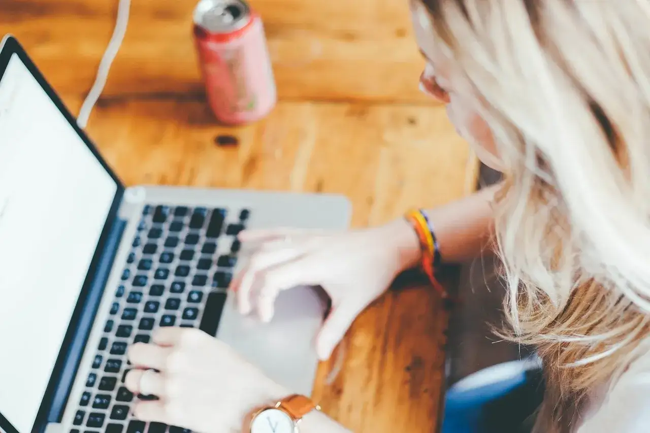 Kobieta z blond włosami pracuje na laptopie, szukając informacji, jak zostać nauczycielem bez studiów pedagogicznych.