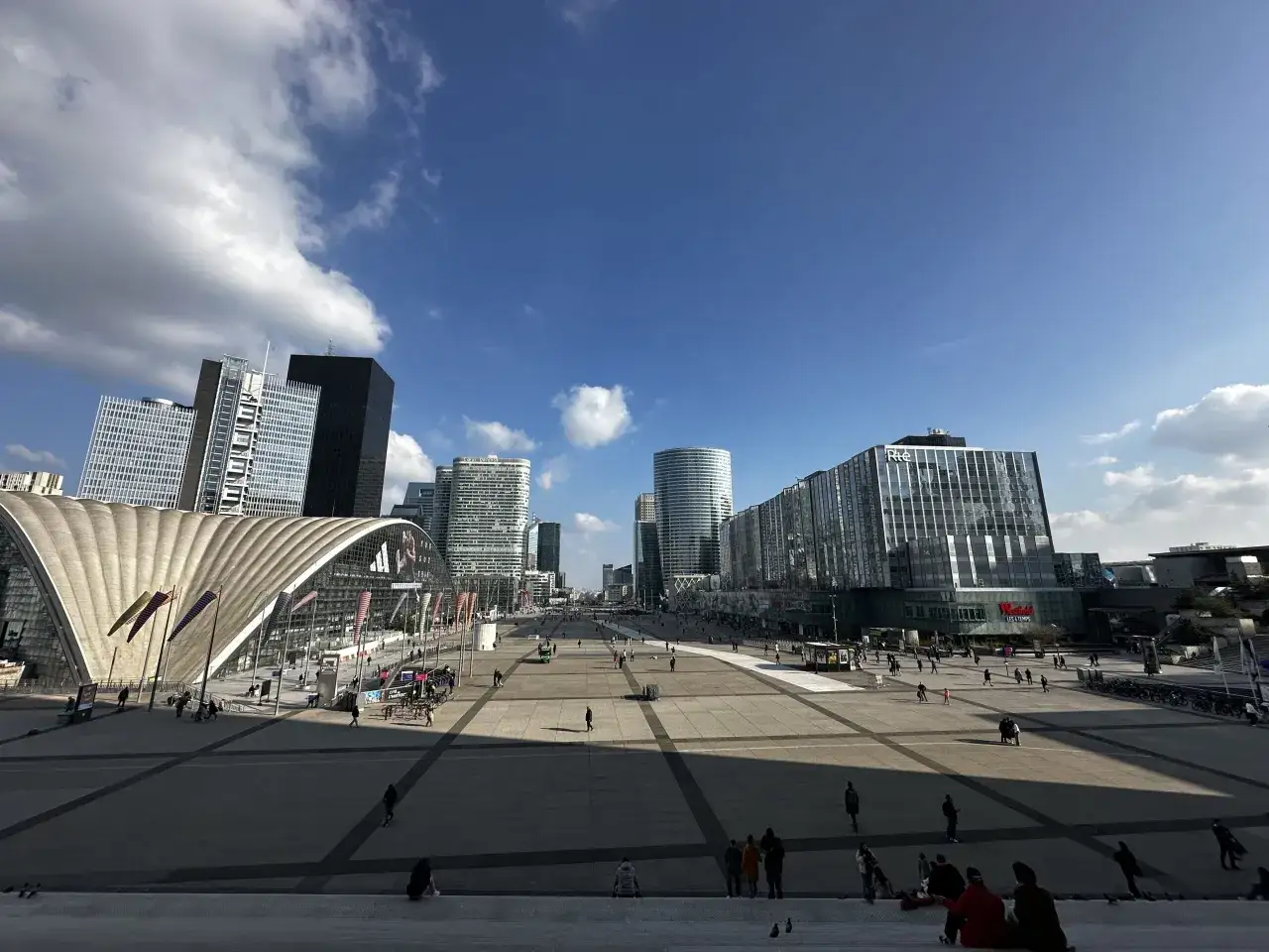 Nowoczesne budynki i szeroki plac w Paryżu po francusku. Słońce i chmury na błękitnym niebie.