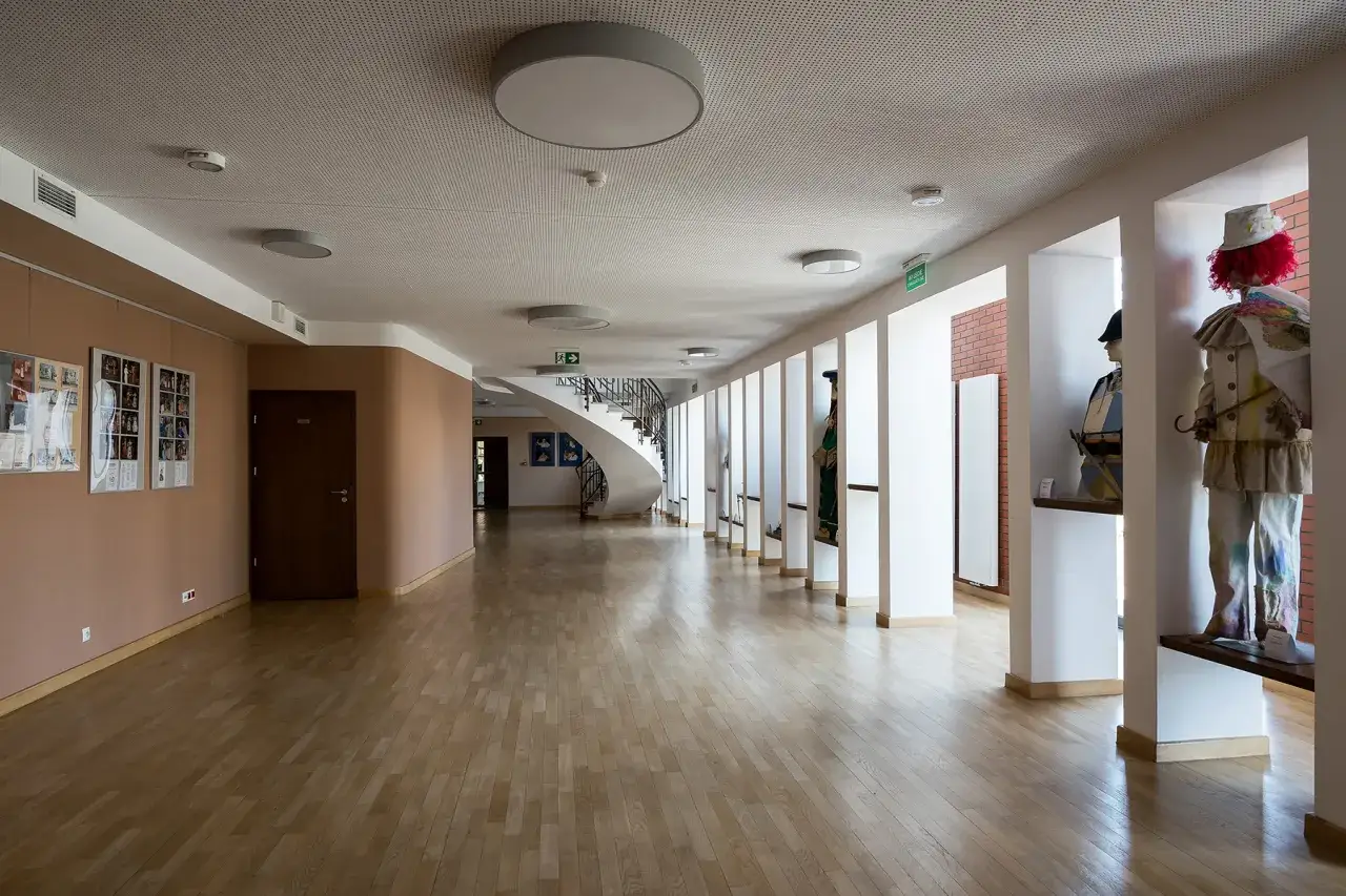 Przestronny foyer z drewnianą podłogą, spiralnymi schodami i manekinami w strojach.