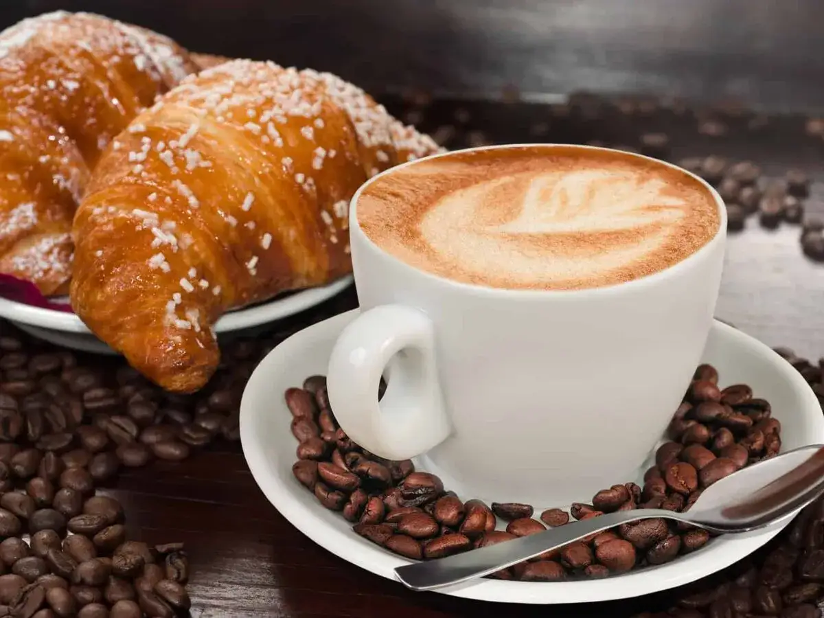 Pyszny rogalik po francusku z kawą latte art i ziarnami kawy. Idealne śniadanie.