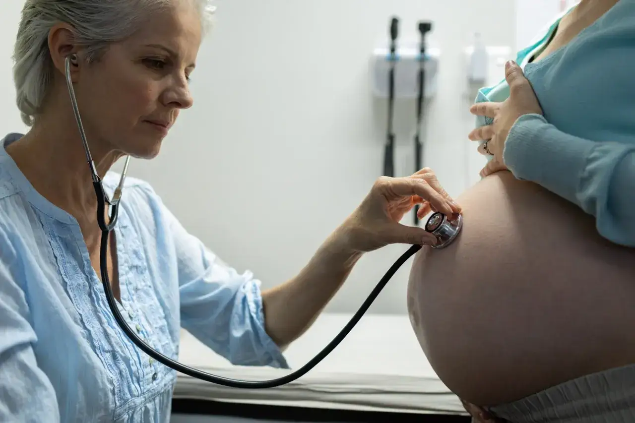 Pielęgniarka osłuchuje brzuch ciężarnej. To badanie, co może podać pielęgniarka bez zlecenia lekarza, by monitorować dobrostan matki i dziecka.